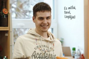 Fotoportrets – jauns smaidīgs puisis īsiem brūniem matiem un baltu hūdiju